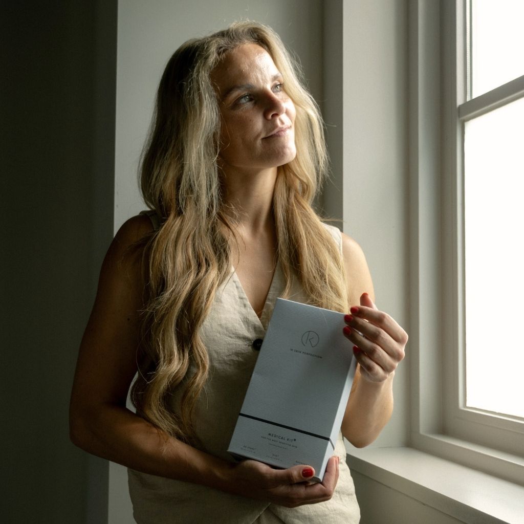 Anouschka kijkt uit het raam terwijl de ze de producten voor huidzorg bij kanker vasthoudt.